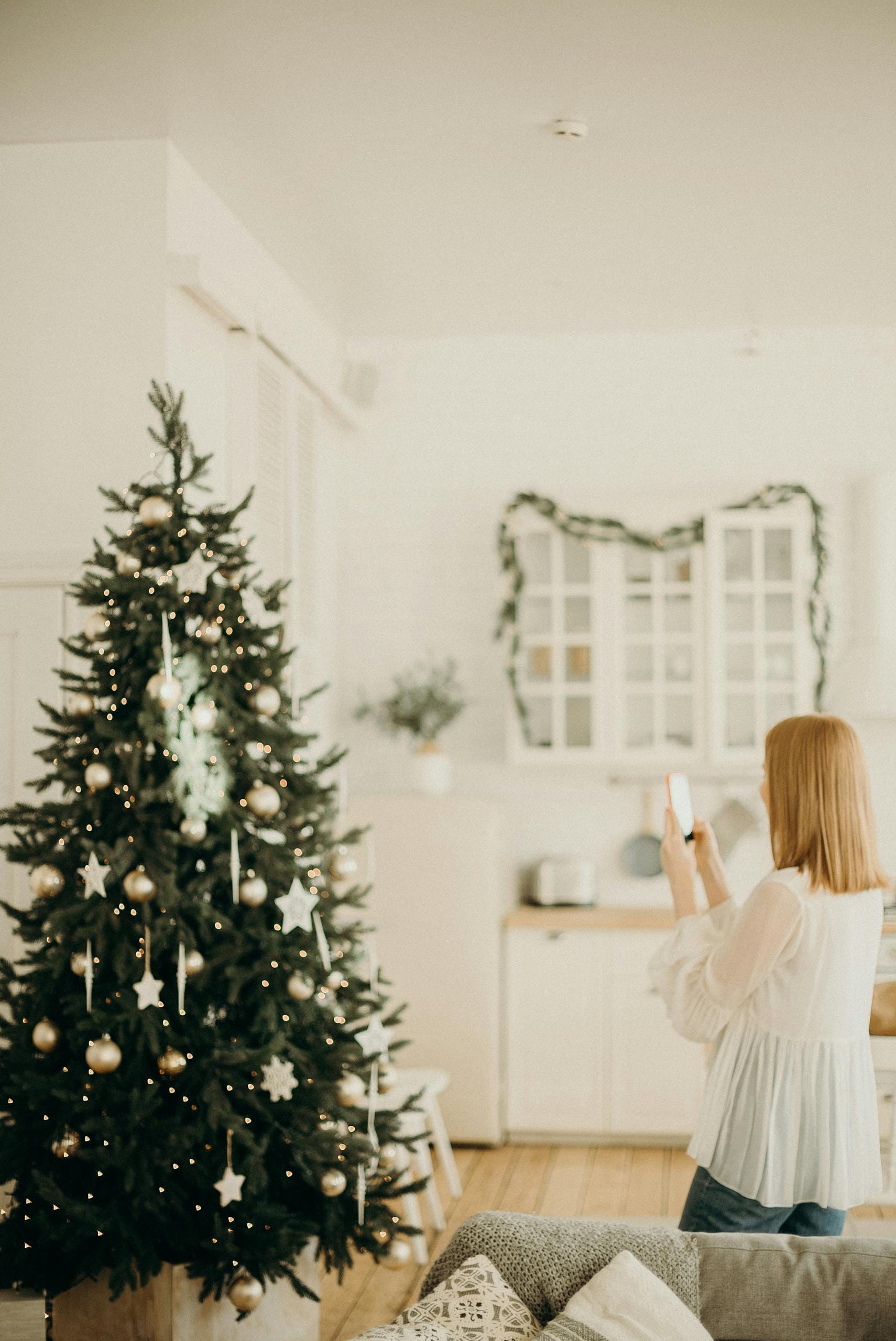 A woman captures a festive Christmas tree indoors, symbolizing holiday cheer.