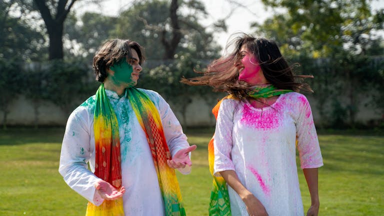 Couple celebrating Holi with colorful powder outdoors, enjoying happy moments together wearing holi outfits, holi clothes.